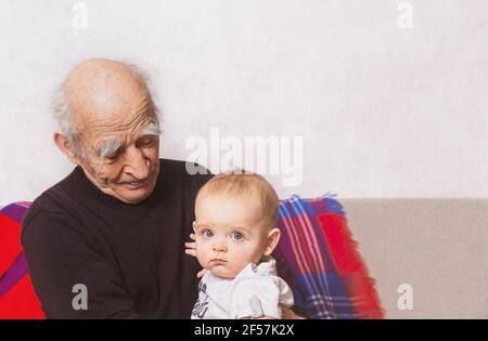 Nonno anziano con nipote seduto sul divano. Uomo che parla con suo nipote. Bisnonno e bisnonno. Nonno sta guardando al bambino. Foto Stock