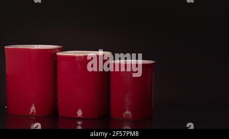 Primo piano di tre tazze rosse di diverse misure su lo sfondo nero Foto Stock