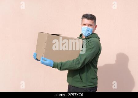 Uomo di consegna in maschera medica e guanti che tengono e trasportano un cartoncino Foto Stock