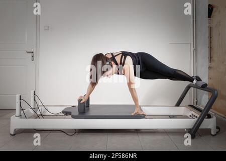Una donna che fa esercizi pilates su un letto riformato. Foto Stock