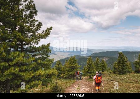 I turisti con zaini scendono dalla cima lungo un bel pendio in una valle di montagna. Attività ricreative e concetto di viaggio. Foto Stock