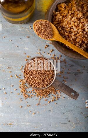 Bulgur Siyez in recipiente di misurazione in metallo su tavolo di legno blu. (Einkorn bulgur) Foto Stock