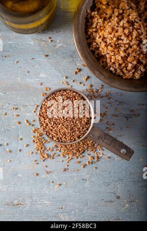 Bulgur Siyez in recipiente di misurazione in metallo su tavolo di legno blu. (Einkorn bulgur) Foto Stock