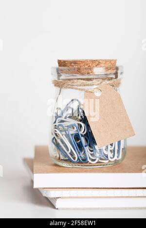 graffette in vaso di vetro con etichetta di carta vuota su una pila di blocchi di blocchi di carta. Spazio di lavoro per ufficio. Mockup per marcare a caldo. Spazio di copia. Concetto di cancelleria per ufficio Foto Stock