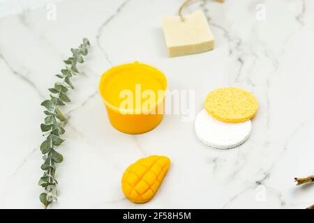 Un mango giallo fatto a mano sapone, un ramo di eucalipto, una spazzola per il massaggio, olio giacciono su un tavolo bianco. Concetto positivo per il corpo Foto Stock