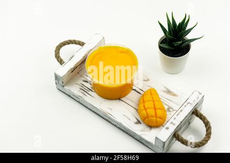 Una mano gialla di mango ha fatto sapone e uno scrub di mango per la cura del corpo, posizionarsi sul vassoio di legno bianco in il bagno moderno Foto Stock