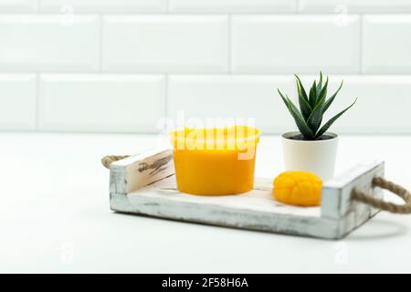 Un mango giallo fatto a mano sapone, un mango scrub e un vaso verde succulente stand su un vassoio di legno in un bagno moderno Foto Stock