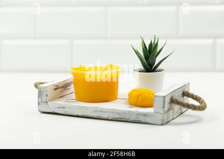Un mango giallo fatto a mano sapone, un mango scrub e un vaso verde succulente stand su un vassoio di legno in un bagno moderno Foto Stock