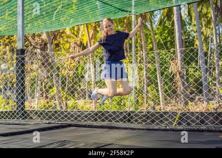 Giovane donna che salta su un trampolino all'aperto, sullo sfondo di palme Foto Stock