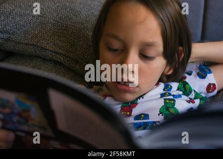 ragazzo della scuola che legge un libro su un divano Foto Stock