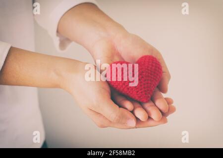 Le donne indossano una maglia a maglia che tiene a mano il cuore rosso. Concetto di amore, speranza, felice Valentino, sanità,donazione di organi,assicurazione, medico, Giornata del cuore del mondo, N. Foto Stock