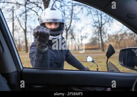 Motociclista arrabbiato bussando con pugno in guanto di pelle nel finestrino laterale dell'auto, vista dall'interno Foto Stock