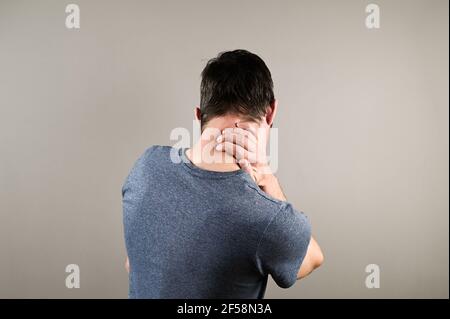 Uomo massaggiando il collo su sfondo grigio. Soffrire di disagio lunghe ore di lavoro sedentario concetto di overworking. Foto di alta qualità Foto Stock