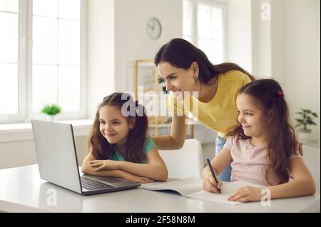 La madre premurosa aiuta i suoi figli a imparare usando un computer portatile per studiare le lezioni scolastiche. Foto Stock