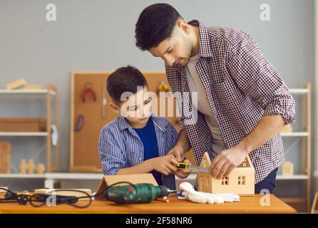 Ragazzino e suo padre che fa modello di casa di legno come parte del progetto di lavoro scolastico Foto Stock