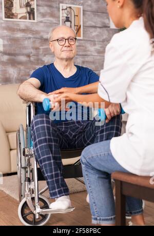 Uomo anziano che cerca di alzare la mano usando i manubri. Anziani disabili con lavoratore sociale in terapia di supporto di recupero fisioterapia sistema sanitario di cura casa di riposo Foto Stock