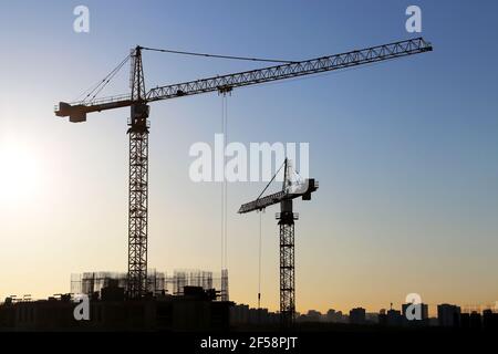 Sagome di gru e edifici da costruzione su sfondo alba. Costruzione di alloggi, condominio in città Foto Stock