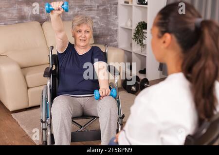 Donna anziana immobilizzata che fa esercizi alle spalle assistiti da infermiere. Disabile anziano ricoverato infermiera di aiuto professionale, cura di casa di riposo e riabilitazione Foto Stock