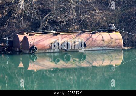 Capiente serbatoio allungato vecchio arrugginito con pneumatici usati per auto usato come protezione paraurti lasciato sul fiume calmo vicino a. riva del fiume coperta di albero Foto Stock