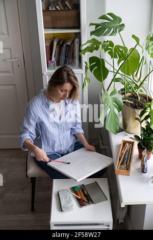 Artista donna dipinge un'immagine su tela, fa schizzi a matita, cancella i segni di gomma con un pennello Foto Stock