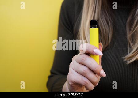 Sigaretta elettronica monouso gialla in mano femminile. Sfondo giallo brillante Foto Stock