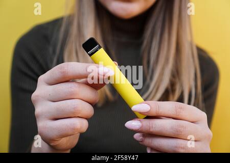 Sigaretta elettronica monouso gialla in mano femminile. Sfondo giallo brillante Foto Stock