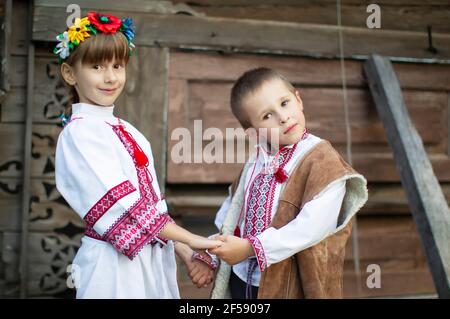 Ragazzino e bambina in abiti nazionali slavi su sfondo ligneo. Bambini bielorussi o ucraini in camicie ricamate. Foto Stock