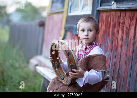 Ragazzino in abito nazionale slavo con un tambourine etnico. Un bambino bielorusso o ucraino in una camicia ricamata con uno strumento musicale folk. Foto Stock