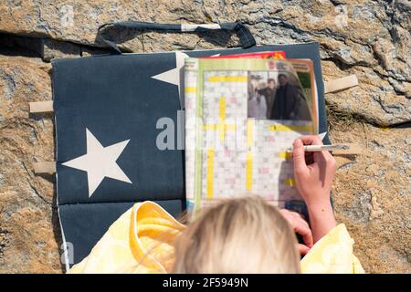 Donna che si rilassa sulla spiaggia risolvendo Crosswords durante la giornata estiva di vacanza. Foto Stock