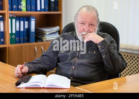 Ritratto di un uomo d'affari anziano penoso seduto alla scrivania nella stanza dell'ufficio, uomo caucasico Foto Stock