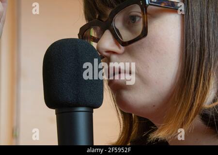 Giovane caucasica bianca che fa un podcast di fronte un microfono Foto Stock