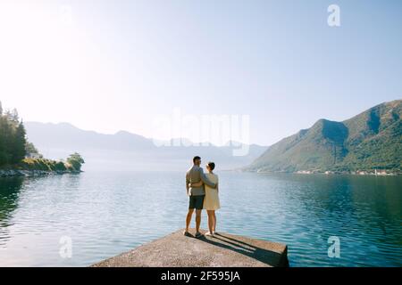 Una coppia innamorata si erge su un molo nella baia di Cattaro vicino Perast sullo sfondo delle montagne, vista posteriore Foto Stock