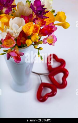 Freesia in vaso e cuori rossi su fondo di legno bianco. Foto Stock
