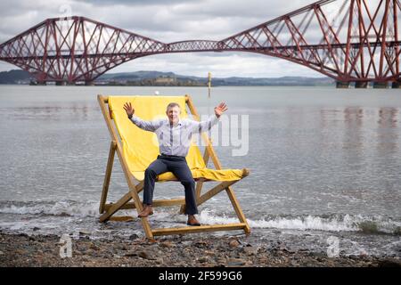 South Queensferry, Scozia, Regno Unito. 25 Marzo 2021. NELLA FOTO: Willie Rennie MSP. Willie Rennie MSP - leader del Partito Liberale democratico Scozzese (Scottish Lib Dems) si è Unito a Rebecca Bell, candidato di Edimburgo Northern e Leith, e a sua figlia Daphne. Legge la figlia di Rebecca un libro su una sedia gigante da spiaggia con la vista del Forth Bridge dietro come parte del loro percorso di campagna elettorale Holyrood per il 6 maggio. Credit: Colin Fisher/Alamy Live News Foto Stock