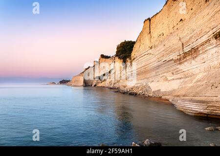 Spiaggia al tramonto di Logas con scogliere bianche a picco sul villaggio di Peroulades sull'isola di Corfù in Grecia. Loggas è famosa per il punto panoramico con vista del mare al tramonto Foto Stock