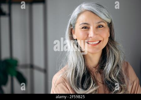 Primo piano ritratto di una donna asiatica d'affari, avvocato, in piedi in ufficio, con capelli grigi maturi e abbastanza fiduciosi, indossando abiti eleganti, guardando la macchina fotografica, sorridente amichevole Foto Stock