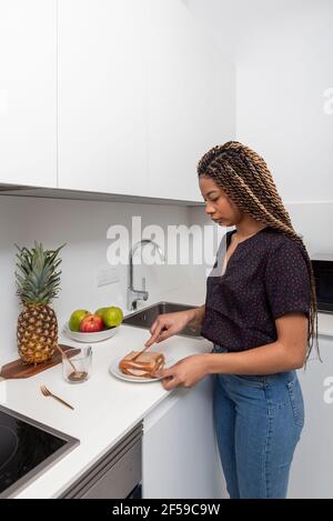 Vista laterale della giovane donna che prepara panini sani per la colazione in una cucina casalinga moderna e leggera Foto Stock
