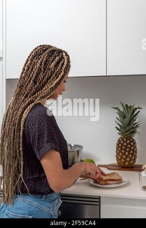 Vista laterale della giovane donna che prepara panini sani per la colazione in una cucina casalinga moderna e leggera Foto Stock