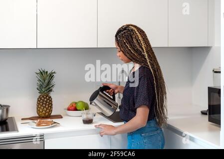 Donna che prepara caffè solubile a casa mentre prepara una colazione sana in cucina casalinga Foto Stock