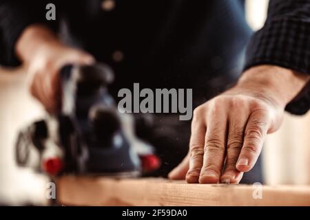 Le mani del falegname che lavora con la pialla elettrica in un'officina Foto Stock