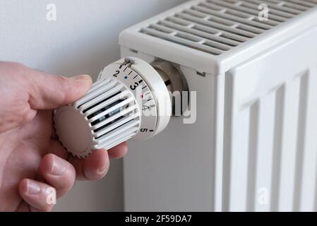 primo piano di una persona che abbassa il termostato sul riscaldatore per risparmiare energia Foto Stock