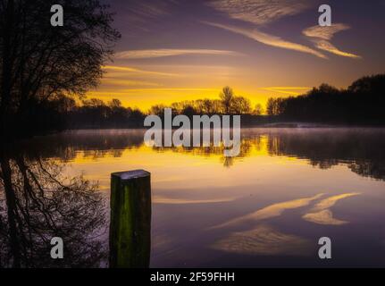 Dawn at Westport Lake in Stoke on Trent, Staffordshire, UK.tranquillo paesaggio mattutino con nebbia ondulata e nuvole colorate che si riflettono in calma Foto Stock