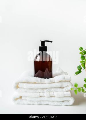 Asciugamani bianchi impilati per il centro benessere e mockup di bottiglie marroni per prodotti da bagno in bagno, shampoo per il centro benessere, gel doccia, sapone liquido su sfondo bianco. Anteriore Foto Stock