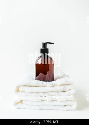 Asciugamani bianchi impilati per il centro benessere e mockup di bottiglie marroni per prodotti da bagno in bagno, shampoo per il centro benessere, gel doccia, sapone liquido su sfondo bianco. Anteriore Foto Stock