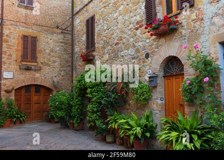 PIENZA, ITALIA - 26 MAGGIO 2017: Bella strada stretta con luce del sole e fiori nel piccolo magico e antico borgo di Pienza, Val D'Orcia Toscana Foto Stock