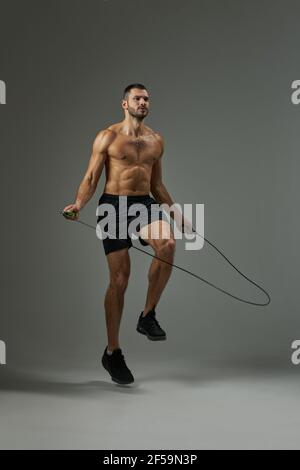 Adorabile atleta con corpo potente in shorts con corda da salto sulla pratica isolato su sfondo grigio Foto Stock