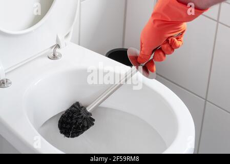 persona che indossa guanti in gomma per la pulizia del recipiente del gabinetto con la spazzola per il gabinetto Foto Stock