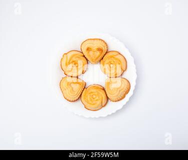 Composizione creativa di muffin appena sfornati in piastra di ceramica bianca, forma a cuore e rosa, concetto di cibo, disposizione piatta, vista dall'alto Foto Stock