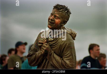 Festival musicale di Glastonbury 1998. Un gaer del festival si trova coperto di fango e immerso nel bagnato presso il sito del festival Foto Stock