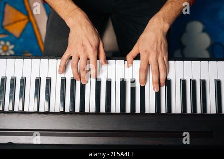 Vista ravvicinata delle mani di un uomo irriconoscibile che suona al pianoforte a casa. Concetto di educazione musicale. Foto Stock